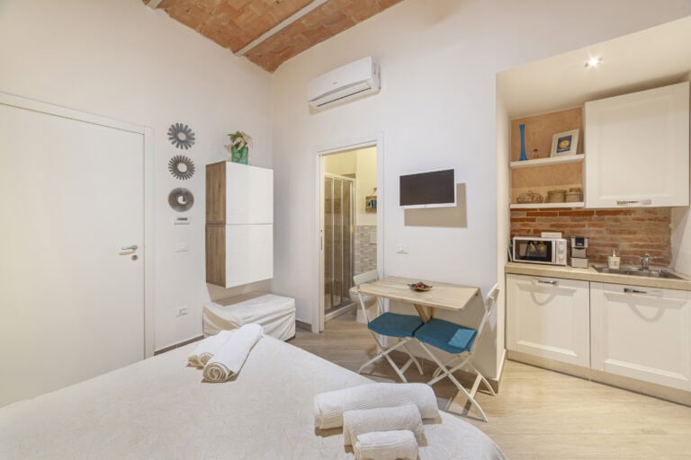 Camera accogliente con letto matrimoniale, angolo cottura e bagno privato, arredata con elementi moderni e dettagli rustici.
