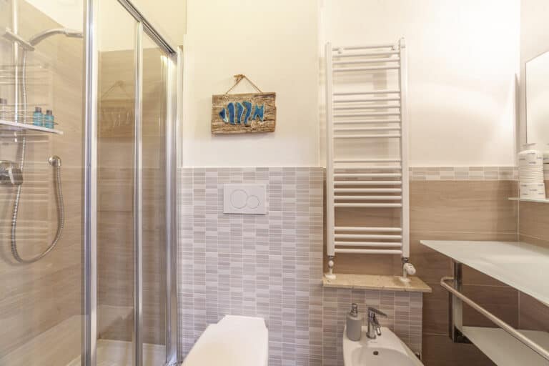 Bagno moderno con box doccia, bidet, scalda salviette e decorazioni a tema marino.