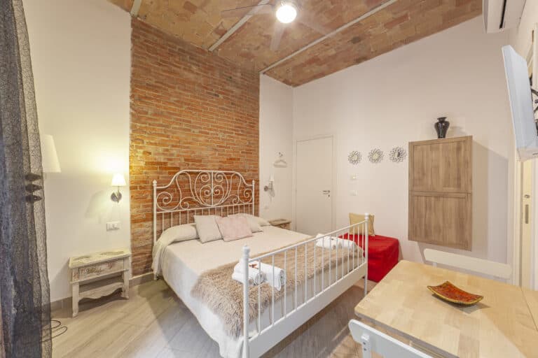 Camera da letto con letto matrimoniale in ferro battuto, parete in mattoni a vista, soffitto in cotto e arredamento in stile rustico.