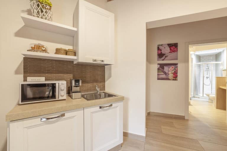 Angolo cottura moderno con lavello, forno a microonde e macchina da caffè, con accesso a un bagno con box doccia.