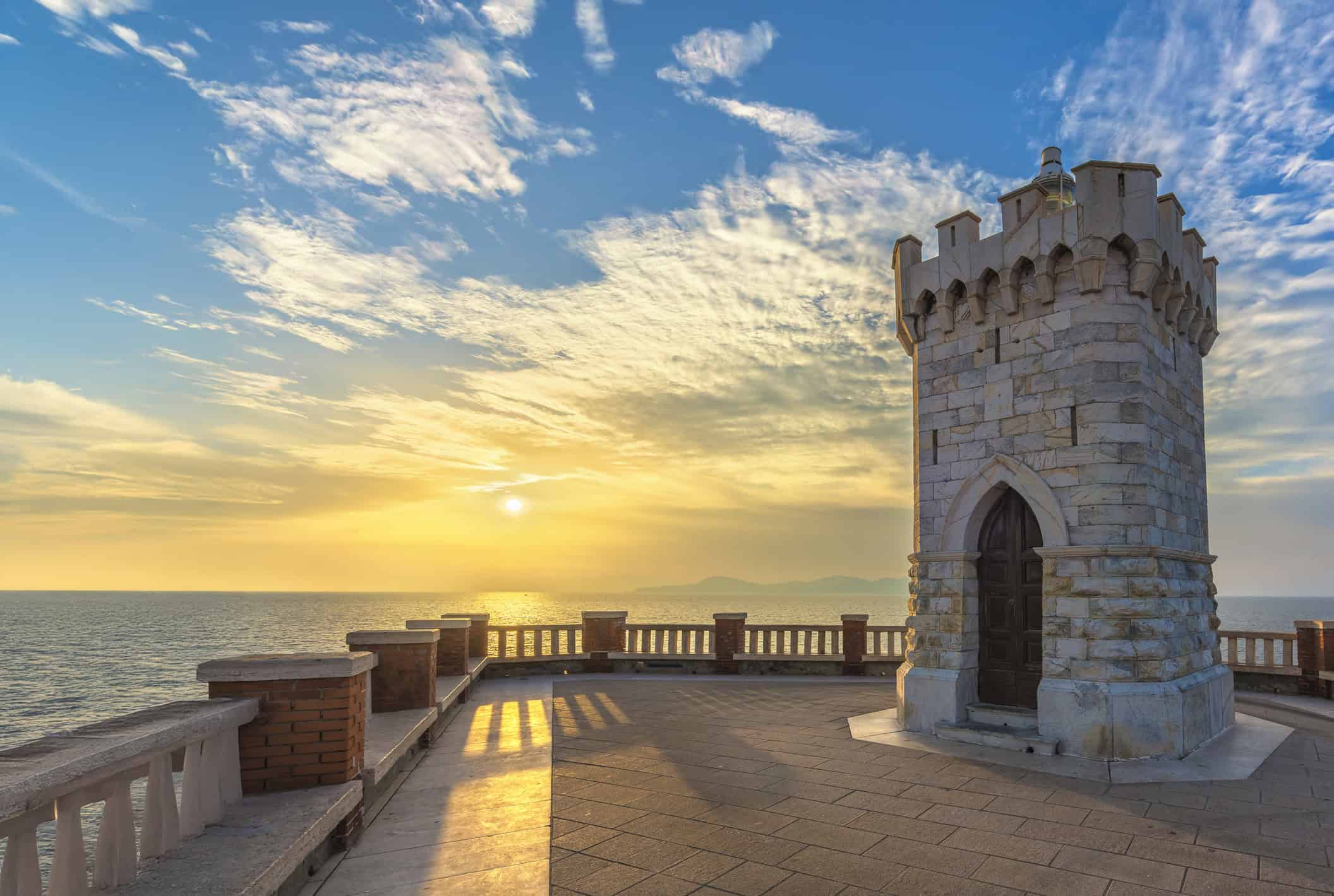 Torre in pietra affacciata sul mare a Piombino, con il sole al tramonto che illumina il cielo e l'acqua, creando un'atmosfera suggestiva.