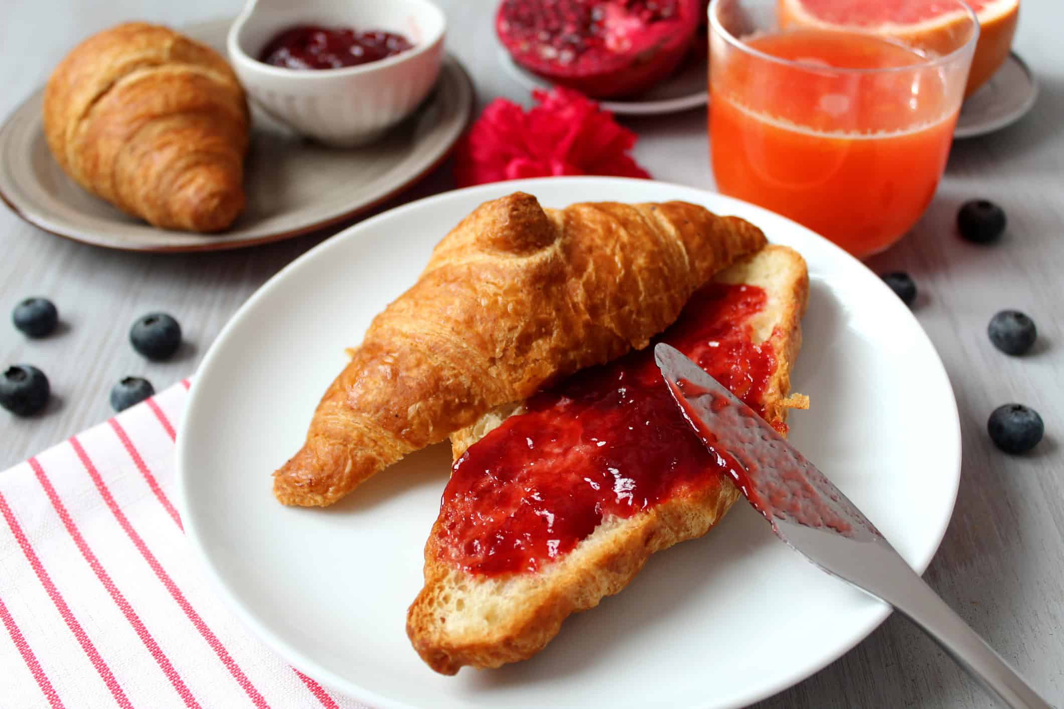 Colazione con croissant e marmellata di fragole, accompagnata da succo d’arancia e frutta fresca